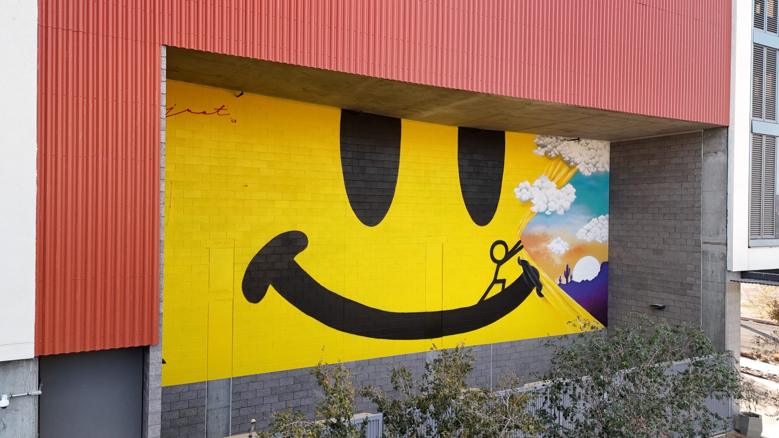 Mural of a smiley face being pulled back by a stick figure to reveal a desert